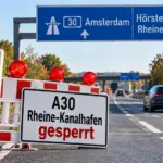 ymbolbild zur A30-Sperrung bei Rheine-Kanalhafen mit Baustellenabsperrung, Warnleuchten und Hinweisschild Richtung Amsterdam und Hörstel.